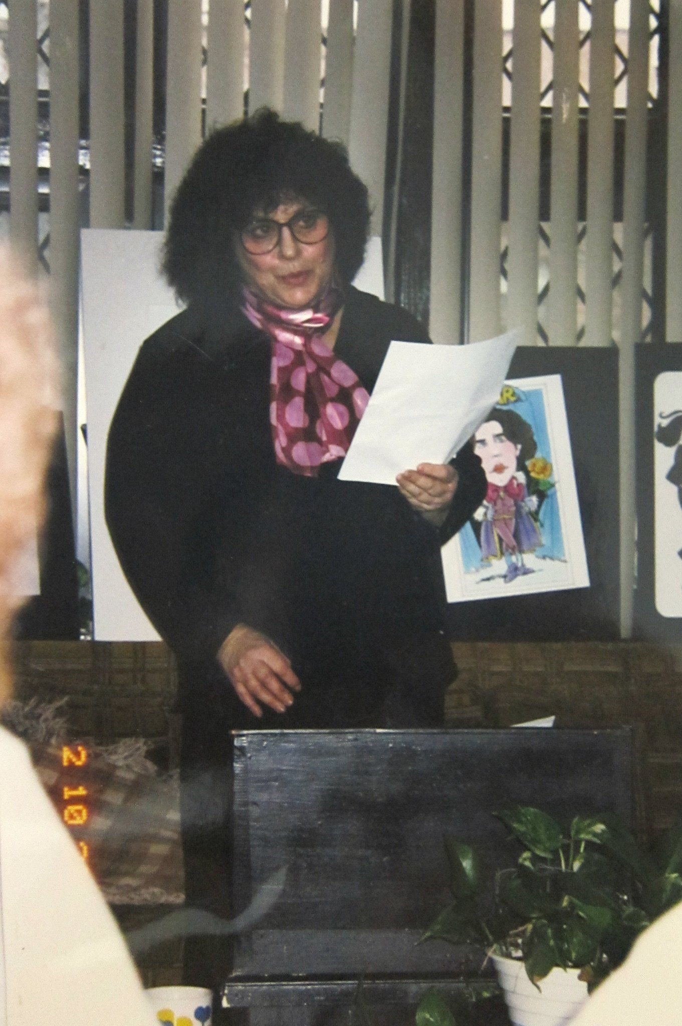 Adele reading from a page, with artwork displayed behind her